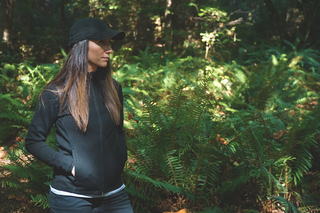 Front three-quarter view of a woman wearing a merino wool Wilderness Expedition full-zip jacket, showing the stand collar, center zipper, long sleeves, hand pockets, and fitted hip-length silhouette